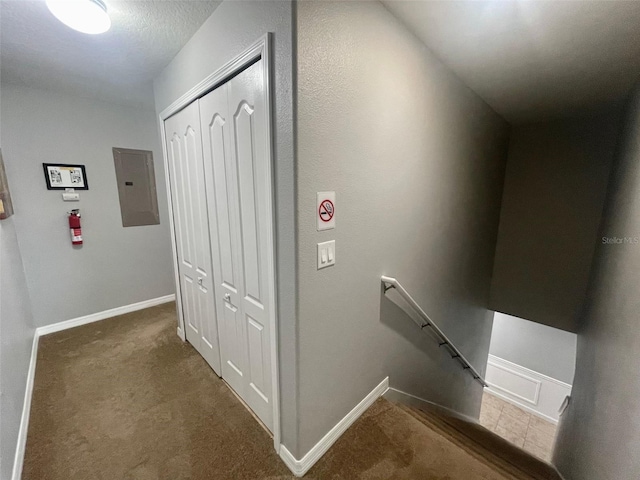 hall with dark carpet, electric panel, and a textured ceiling