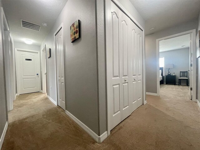 corridor featuring light carpet and a textured ceiling