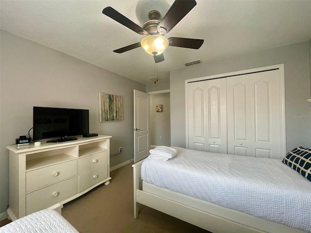 bedroom with a textured ceiling, dark carpet, ceiling fan, and a closet