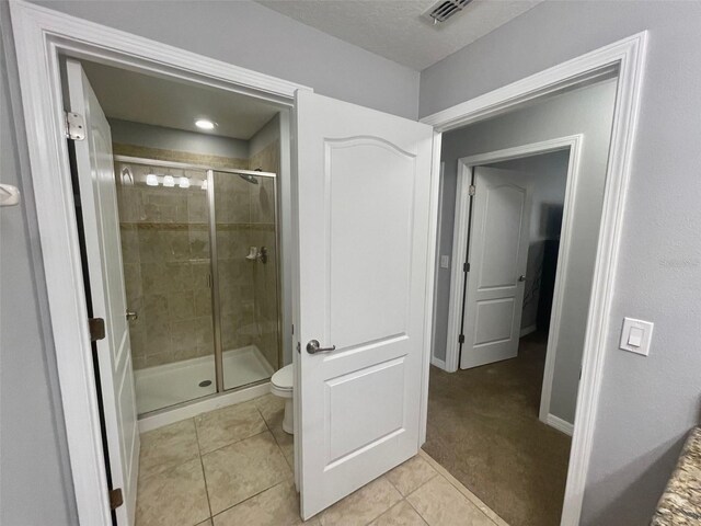 bathroom featuring tile patterned flooring, toilet, and an enclosed shower