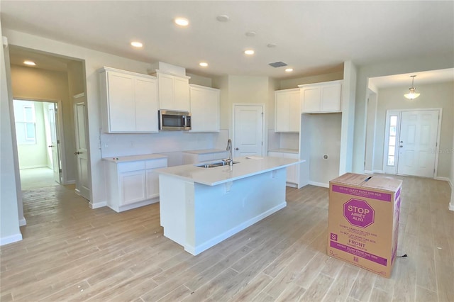 kitchen featuring pendant lighting, white cabinetry, an island with sink, sink, and light wood-type flooring