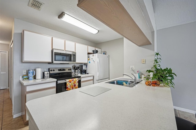 kitchen with white cabinets, light tile patterned flooring, sink, kitchen peninsula, and appliances with stainless steel finishes