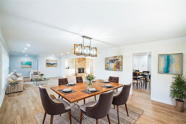 dining area with a stone fireplace, crown molding, light hardwood / wood-style flooring, and a chandelier