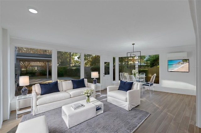 living room featuring an AC wall unit, wood-type flooring, and an inviting chandelier