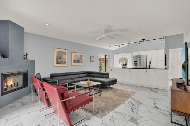 living room with a textured ceiling, track lighting, sink, a brick fireplace, and ceiling fan