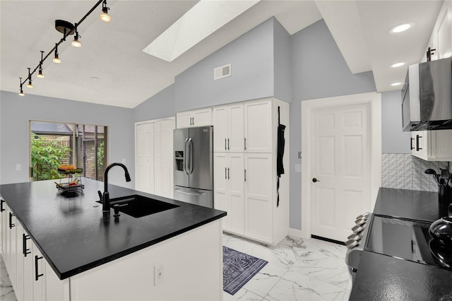 kitchen featuring decorative backsplash, white cabinetry, lofted ceiling with skylight, stainless steel refrigerator with ice dispenser, and sink