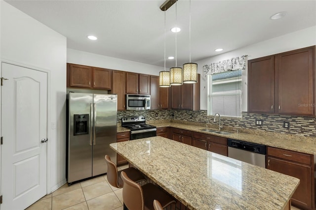 kitchen with decorative light fixtures, appliances with stainless steel finishes, light stone countertops, sink, and a kitchen island