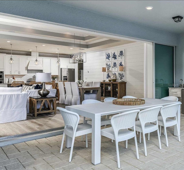 dining space with light hardwood / wood-style flooring, a raised ceiling, an inviting chandelier, and ornamental molding