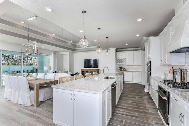 kitchen with decorative light fixtures, a large island with sink, white cabinetry, a tray ceiling, and dark wood-type flooring