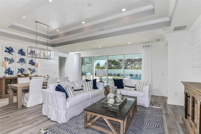 living room featuring hardwood / wood-style floors, a chandelier, a raised ceiling, and crown molding