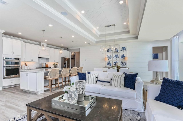 living room featuring light wood-type flooring, a raised ceiling, a notable chandelier, and ornamental molding