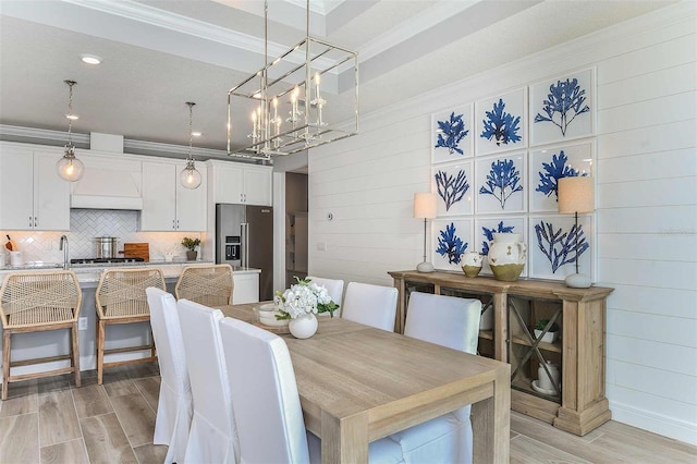 dining space featuring sink, wood walls, light hardwood / wood-style floors, and ornamental molding