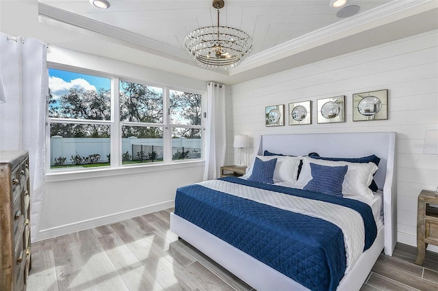 bedroom featuring wooden walls, an inviting chandelier, crown molding, hardwood / wood-style floors, and a raised ceiling