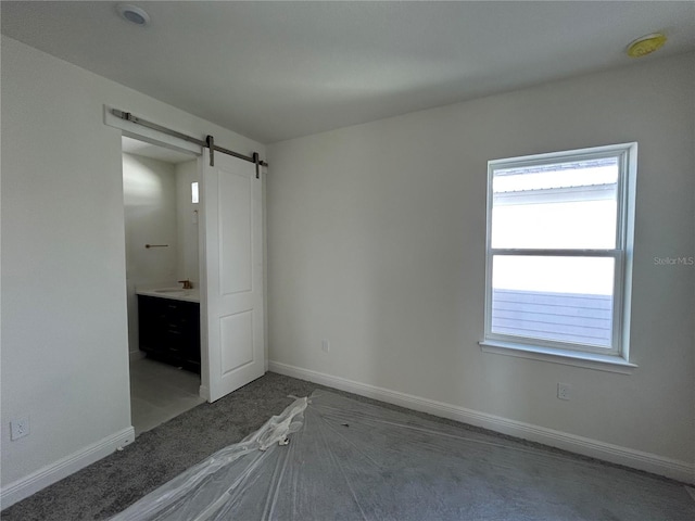 unfurnished bedroom with ensuite bathroom, a barn door, and sink