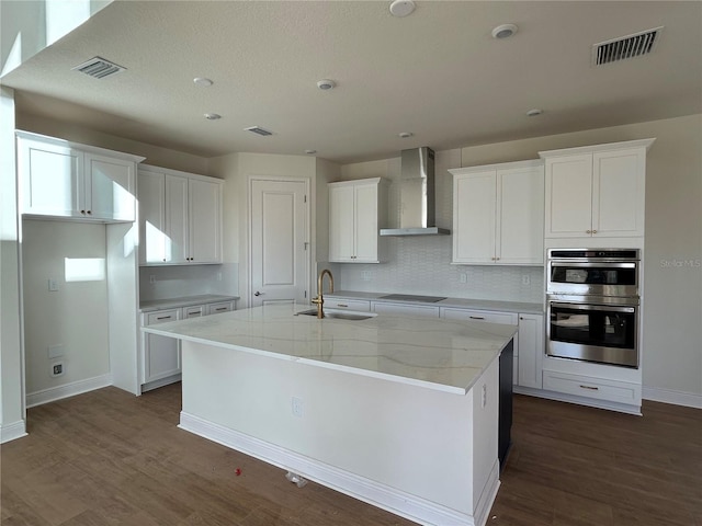 kitchen featuring white cabinetry, wall chimney range hood, sink, and a center island with sink