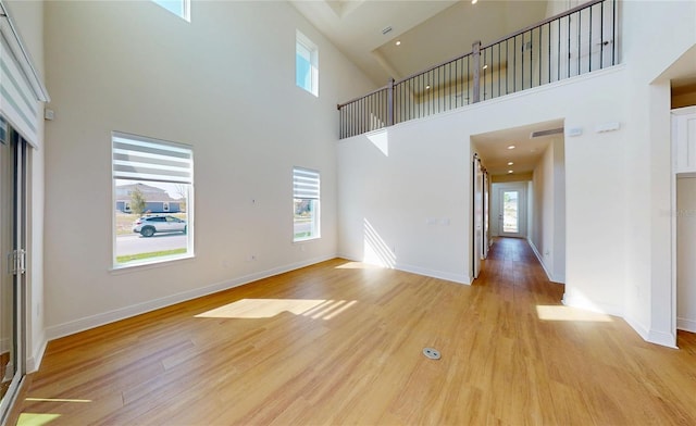 unfurnished living room with light wood-type flooring, visible vents, a high ceiling, and baseboards