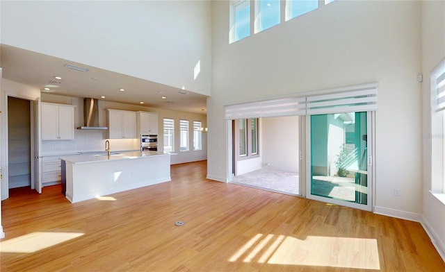 unfurnished living room featuring light wood-style flooring, a high ceiling, a sink, visible vents, and baseboards