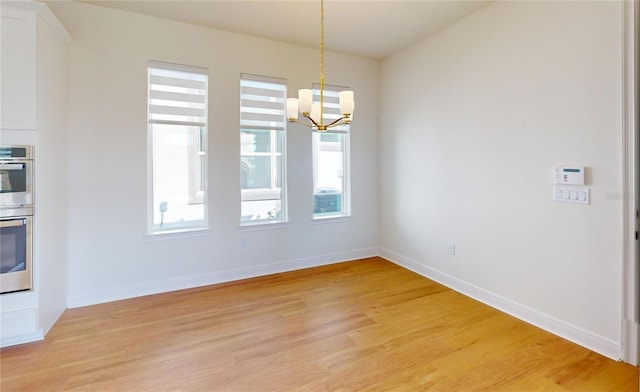 unfurnished dining area featuring baseboards, light wood finished floors, and an inviting chandelier