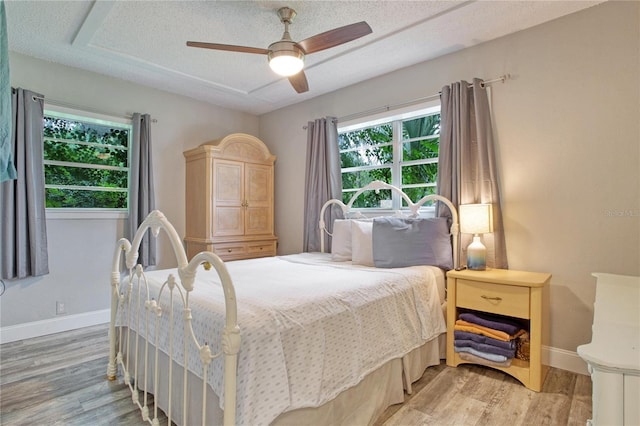 bedroom with light wood-type flooring, multiple windows, ceiling fan, and a textured ceiling