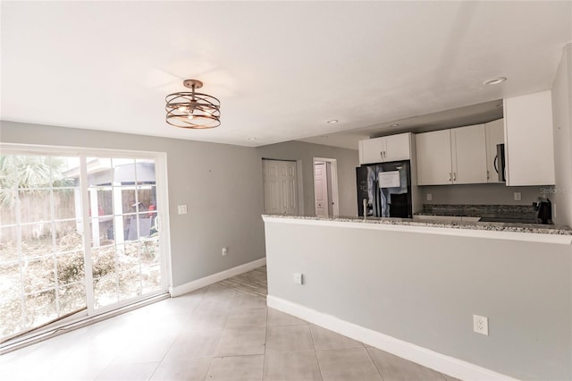 kitchen featuring white cabinets, kitchen peninsula, black fridge, and light stone countertops