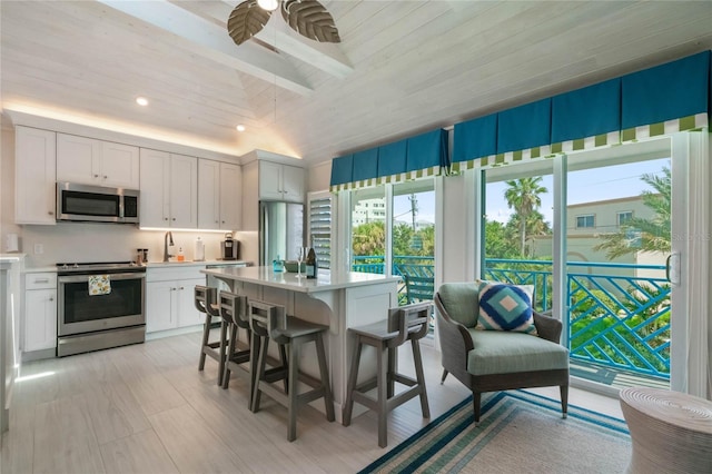 kitchen with light countertops, a kitchen bar, stainless steel appliances, ceiling fan, and white cabinets