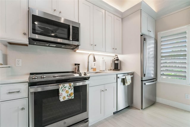 kitchen featuring crown molding, stainless steel appliances, sink, white cabinetry, and light wood-type flooring