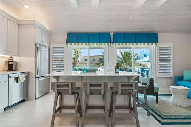 kitchen with light countertops, a kitchen island, a breakfast bar, appliances with stainless steel finishes, and white cabinets