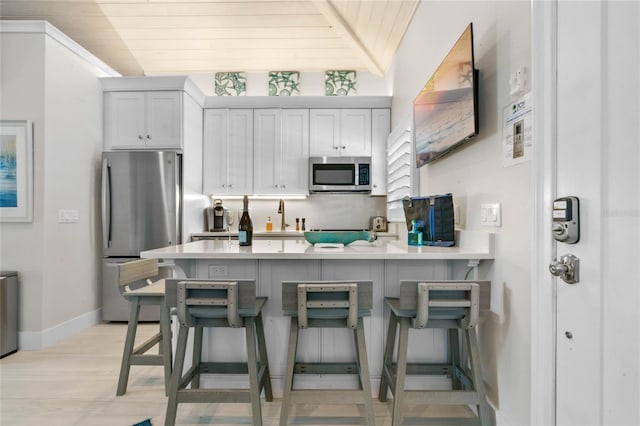 kitchen featuring wooden ceiling, appliances with stainless steel finishes, light wood-type flooring, and a kitchen breakfast bar