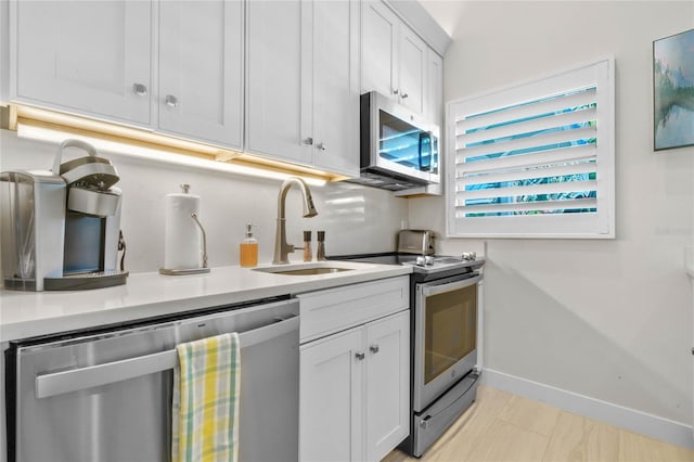 kitchen with white cabinetry, light countertops, baseboards, a sink, and appliances with stainless steel finishes