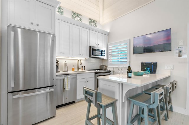 kitchen featuring light countertops, a sink, a kitchen bar, a peninsula, and stainless steel appliances