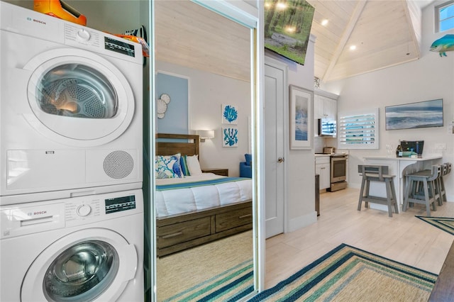 laundry area featuring a towering ceiling, stacked washer and clothes dryer, wooden ceiling, and light hardwood / wood-style flooring