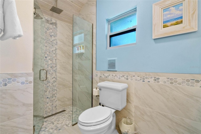 full bathroom featuring tile walls, a wainscoted wall, visible vents, a shower stall, and toilet