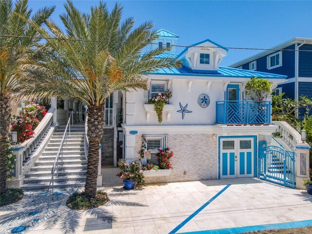 view of front of home featuring stairway, french doors, stucco siding, a balcony, and metal roof
