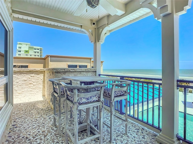 view of patio / terrace featuring a balcony, a water view, a bar, a beach view, and ceiling fan