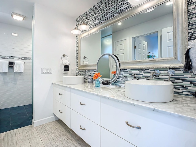 bathroom featuring double vanity, a sink, tasteful backsplash, and baseboards