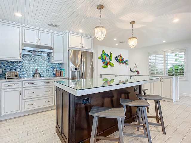 kitchen with white cabinets, hanging light fixtures, a notable chandelier, stainless steel refrigerator with ice dispenser, and a kitchen island