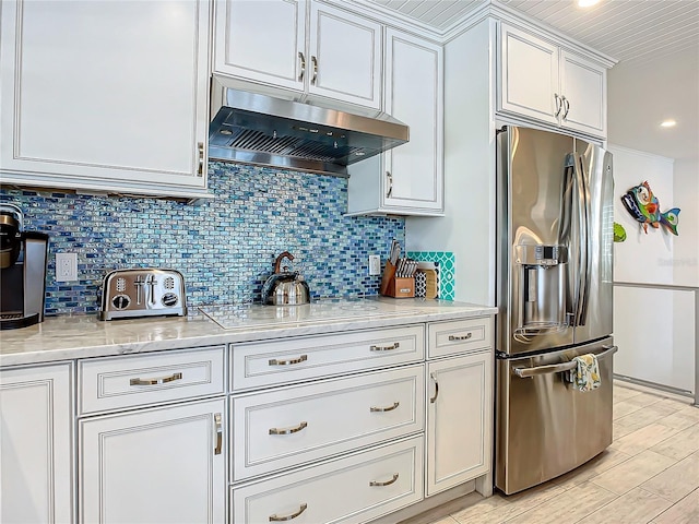 kitchen featuring white cabinets, stovetop, light stone counters, stainless steel fridge, and tasteful backsplash