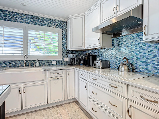kitchen featuring black electric stovetop, under cabinet range hood, backsplash, a sink, and white cabinets