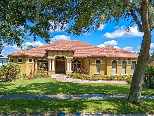 mediterranean / spanish house featuring stucco siding, a tiled roof, and a front yard