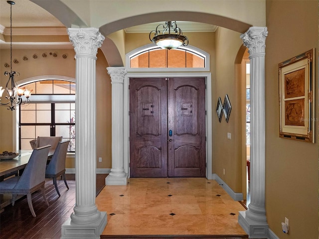 entrance foyer featuring crown molding, a notable chandelier, arched walkways, a wealth of natural light, and ornate columns
