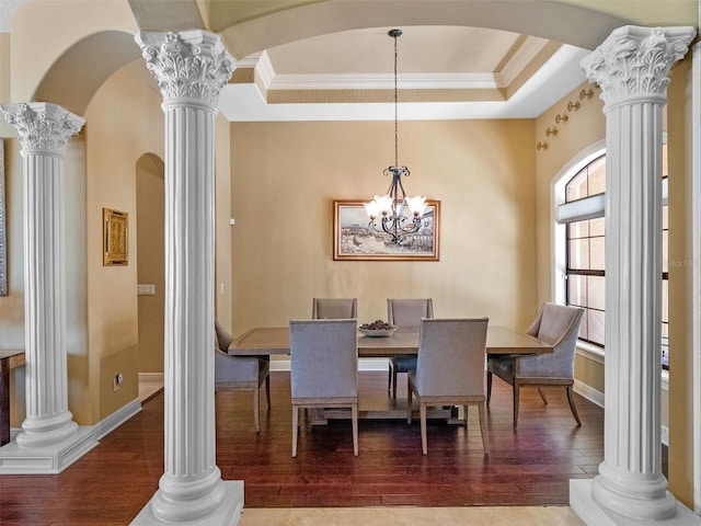 dining space featuring crown molding, a raised ceiling, arched walkways, wood finished floors, and ornate columns