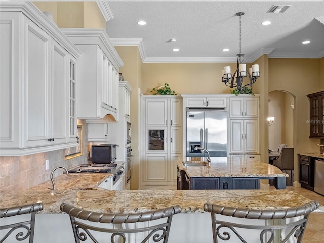 kitchen with visible vents, built in appliances, a kitchen breakfast bar, arched walkways, and a sink