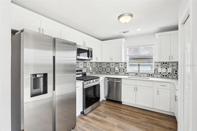 kitchen with backsplash, wood-type flooring, stainless steel appliances, sink, and white cabinets