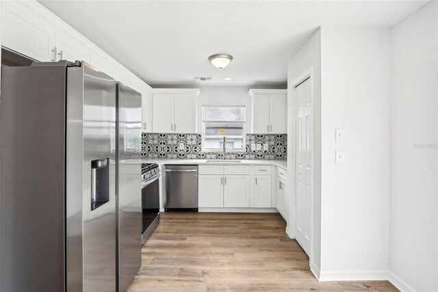 kitchen with light hardwood / wood-style flooring, appliances with stainless steel finishes, tasteful backsplash, sink, and white cabinets