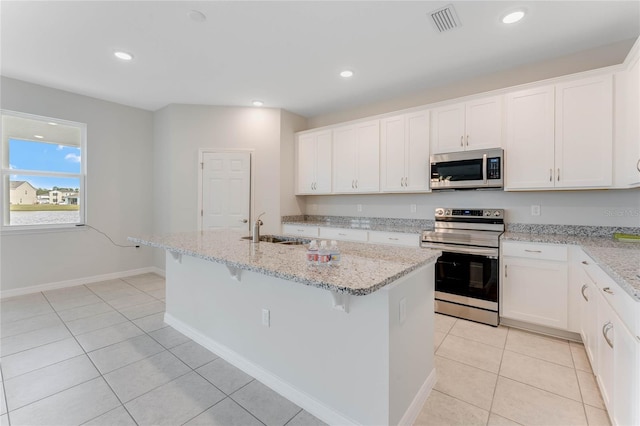 kitchen with light stone countertops, a kitchen island with sink, stainless steel appliances, sink, and white cabinetry