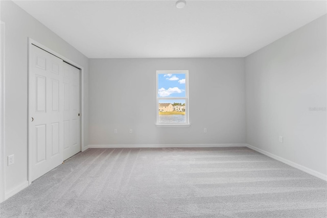 unfurnished bedroom featuring baseboards, a closet, and light carpet