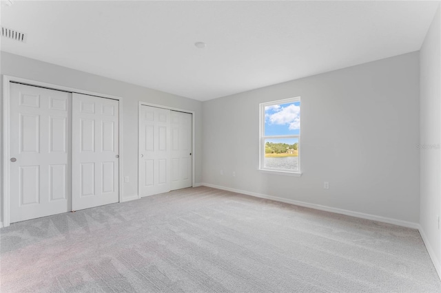 unfurnished bedroom featuring two closets and light carpet