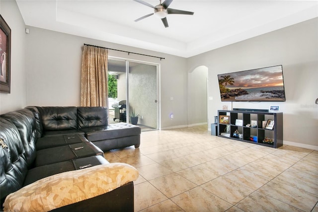 living room featuring a tray ceiling, light tile patterned floors, and ceiling fan