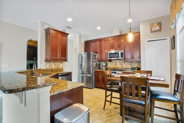 kitchen featuring appliances with stainless steel finishes, sink, kitchen peninsula, dark stone counters, and decorative light fixtures