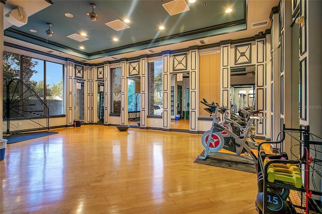 exercise room with light hardwood / wood-style floors, ornamental molding, and a tray ceiling